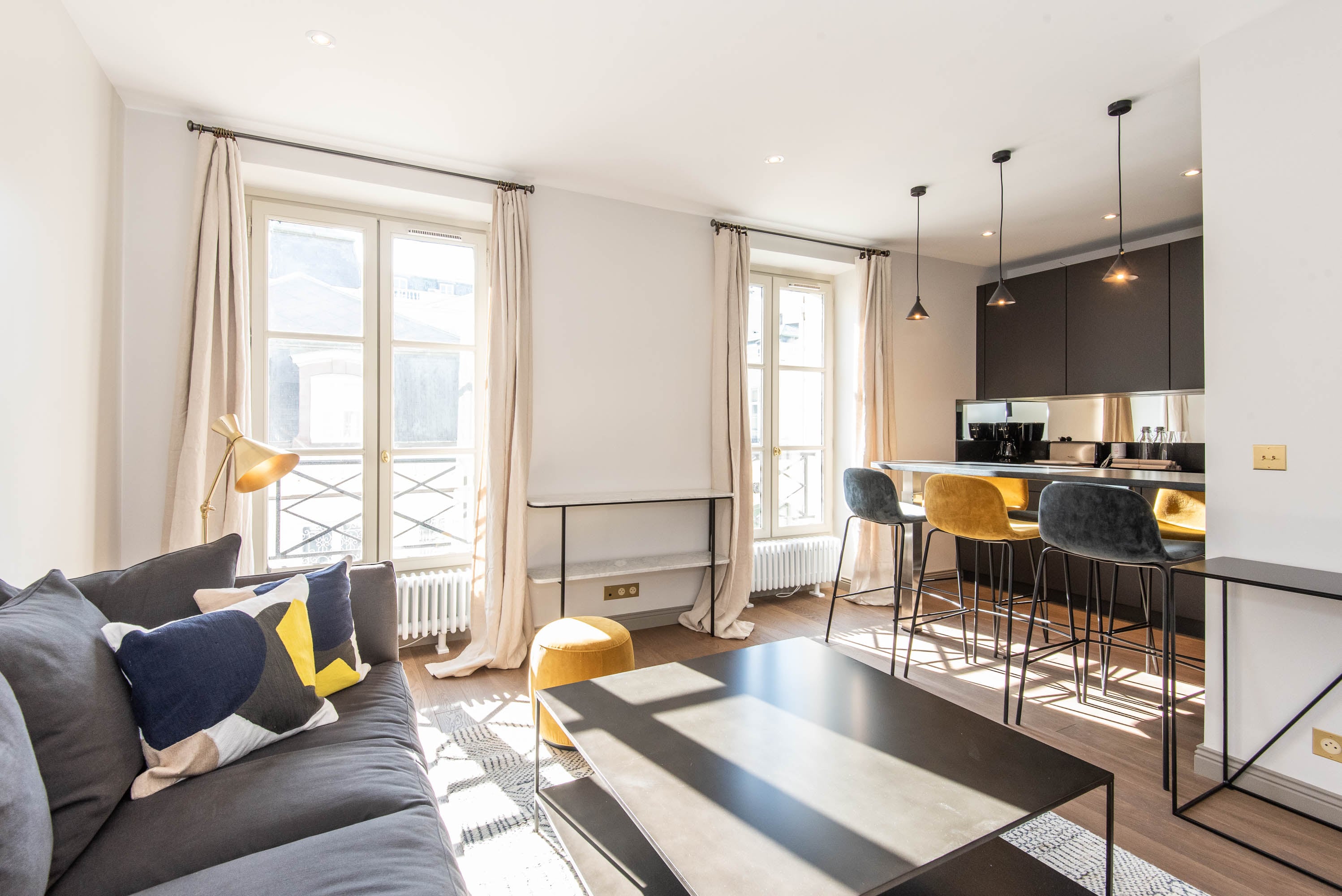 Luminous open-plan apartment featuring floor-to-ceiling windows, contemporary black kitchen, elegant pendant lighting, and sophisticated living space with premium finishes.