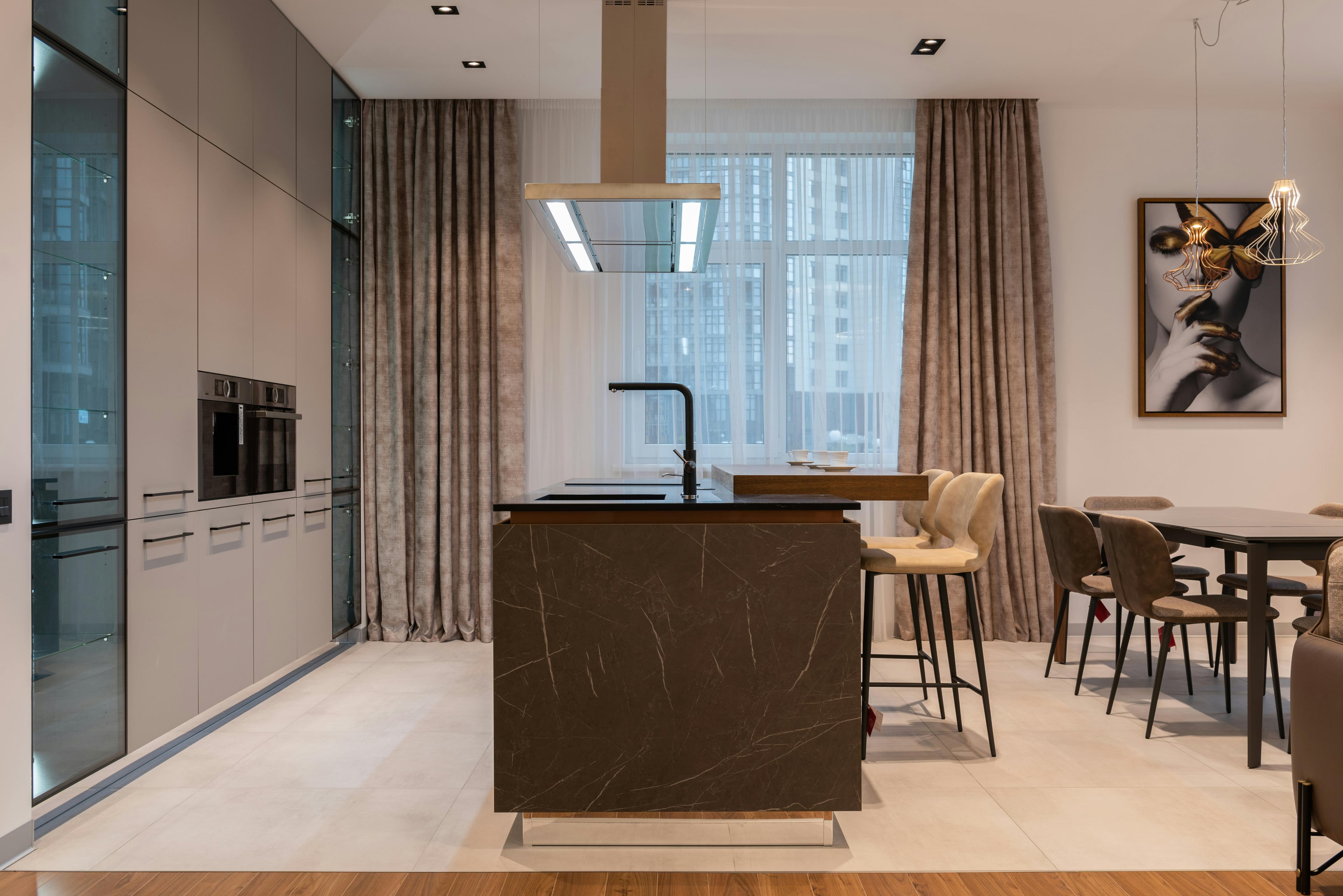 Luxury open-plan kitchen with marble island, floor-to-ceiling windows, premium appliances, and panoramic city views. Contemporary design with natural light and sophisticated finishes.